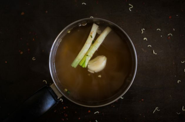 Come preparare il ramen fatto in casa: portare a ebollizione il brodo e inserire uno spicchio d'aglio, lo zenzero sbucciato e i gambi di cipolla verde